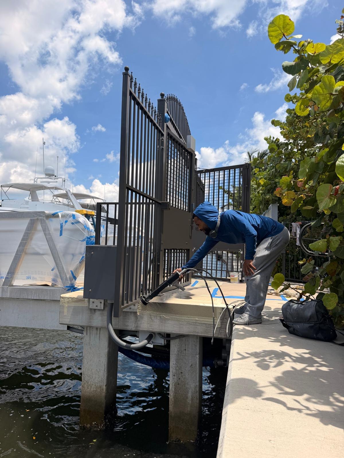 Technician applying electrostatic coating to a waterfront metal gate in South Florida