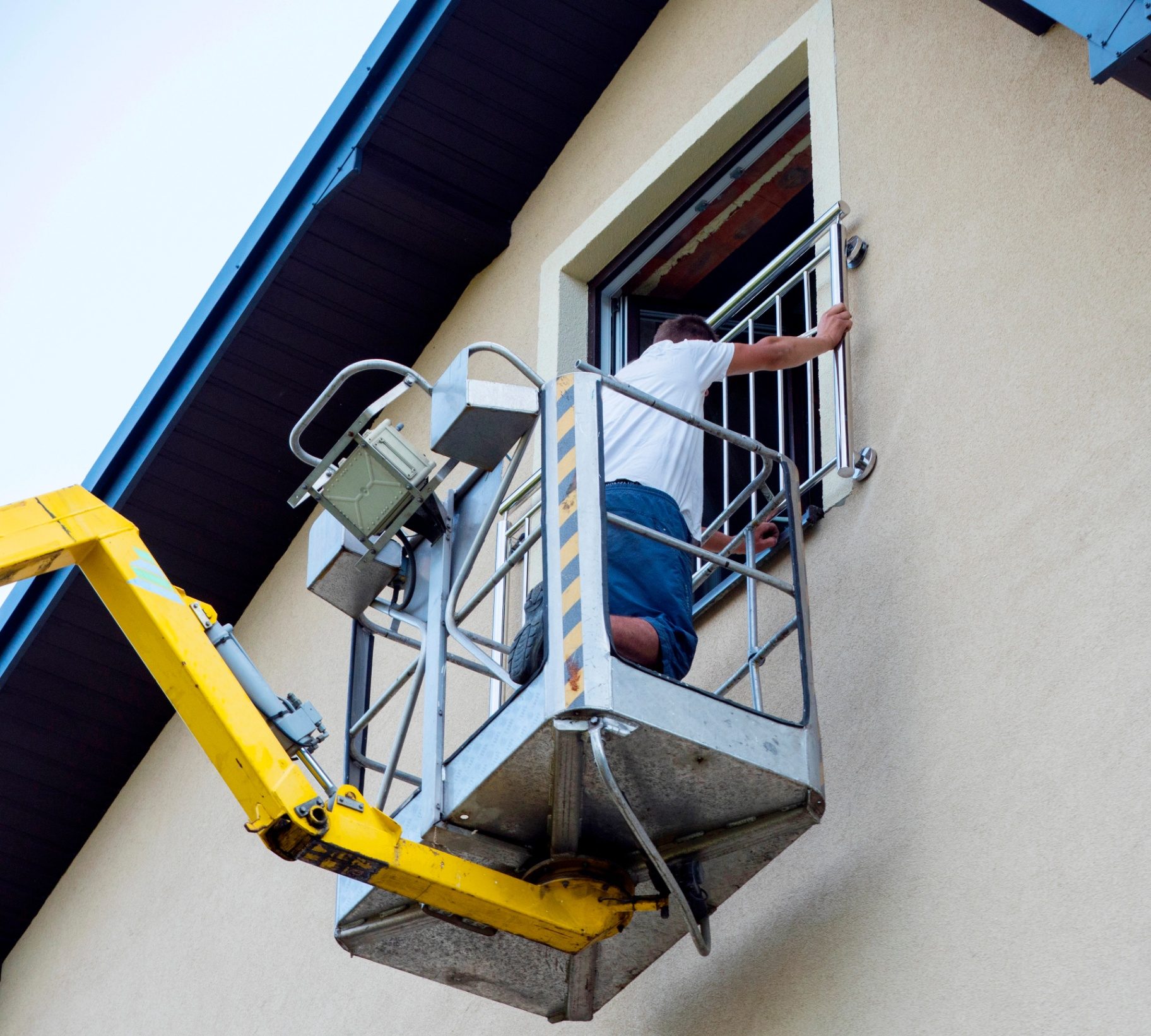 Technician refinishing installed metal railing from a lift on an exterior building elevation